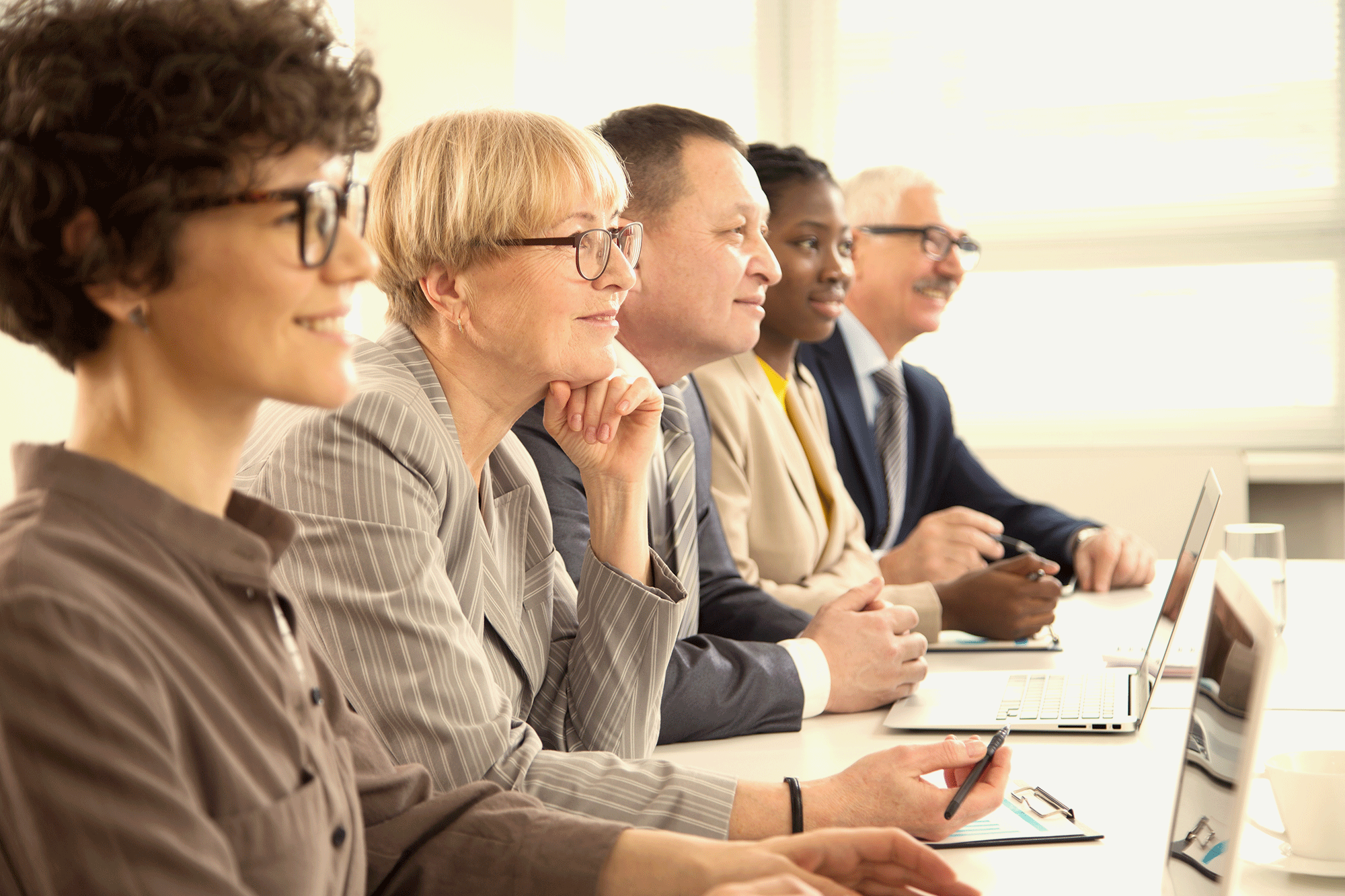 a diverse group of smiling mid-career professionals sit in a row in a classroom