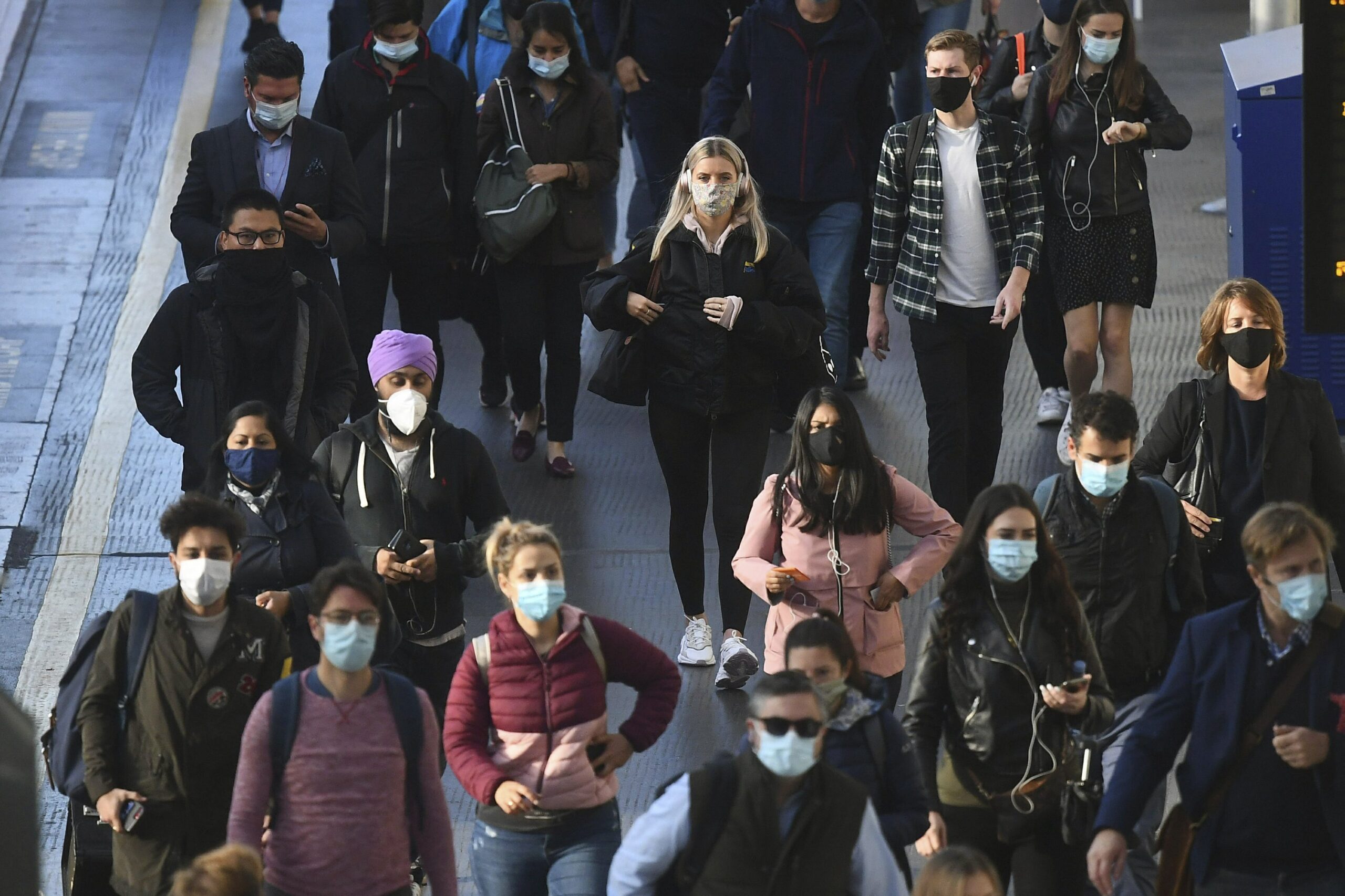 crowd of workers wearing masks walks down a sidewalk