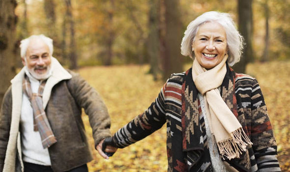 a smiling retired couple walks in the woods