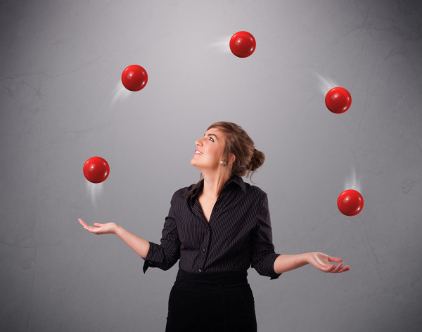 a woman wearing a black blouse and skirt smiles as she juggles five red balls in the air