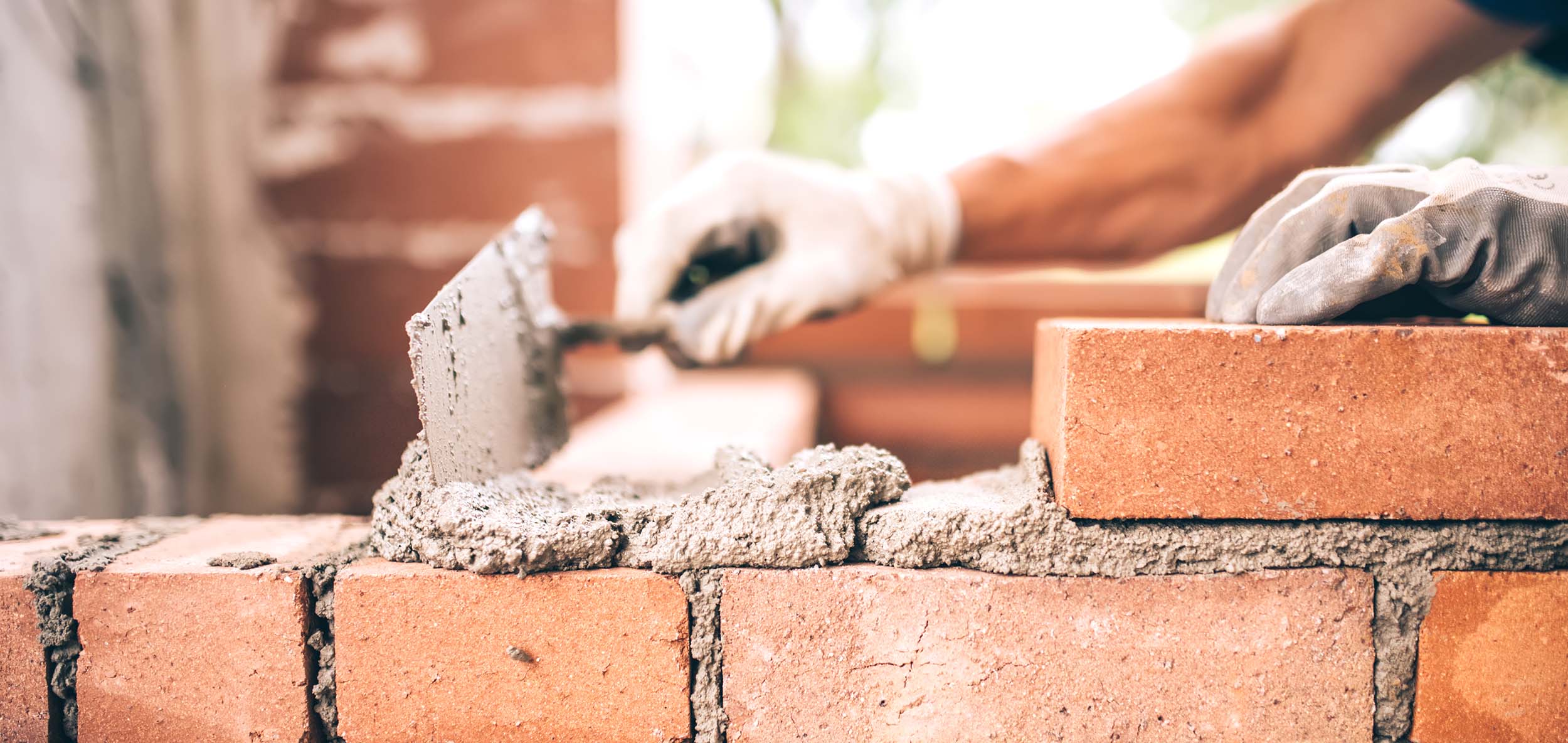 closeup of hands spreading mortar with a trowel and laying bricks for a foundation wall