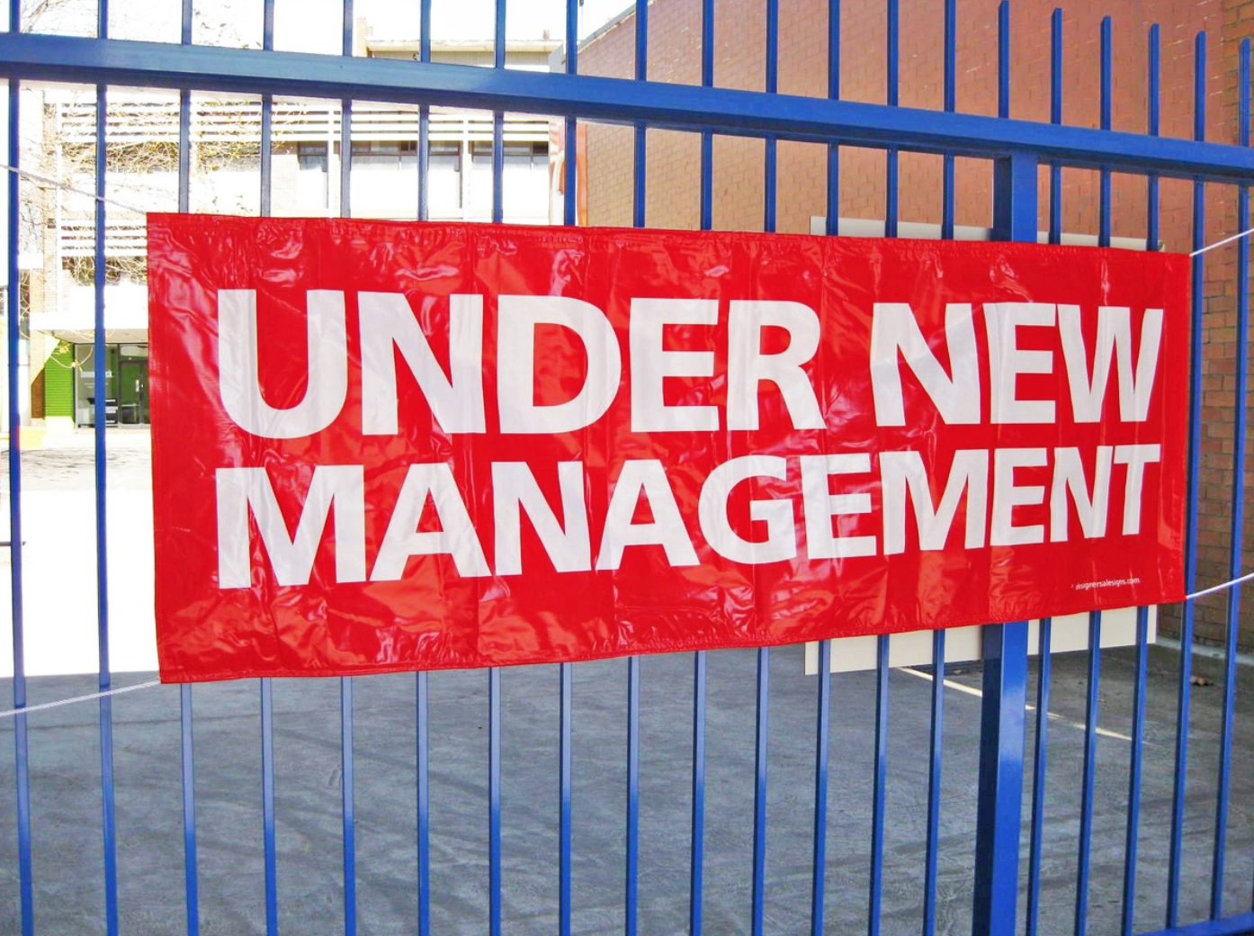 red "under new management" sign hanging on a blue fence