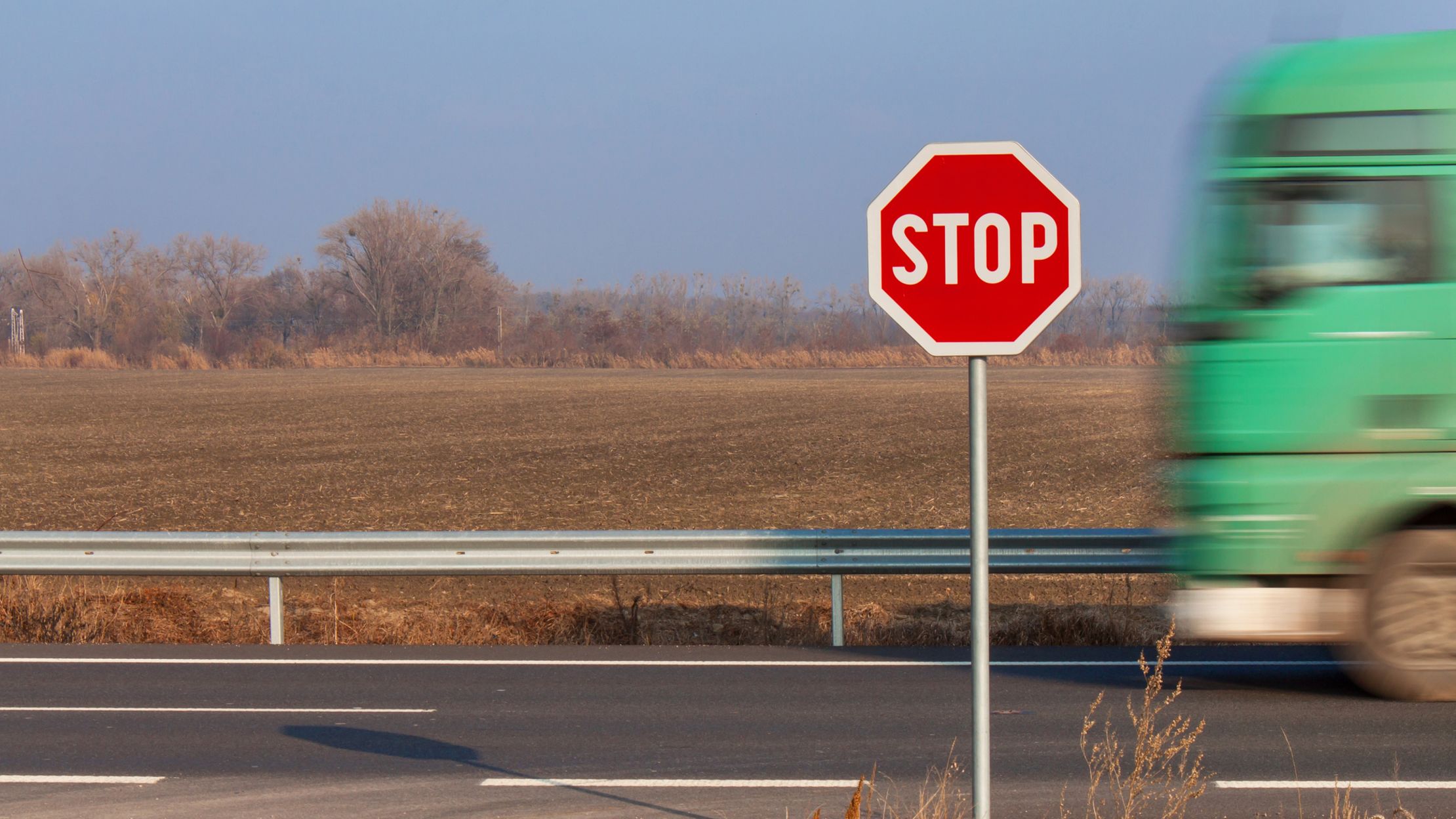 a stop sign stands near a road and field while a bus drives by