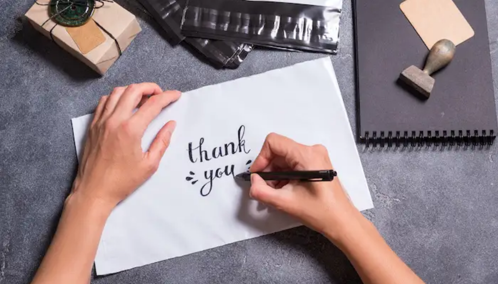 two hands write the words "thank you" on a card