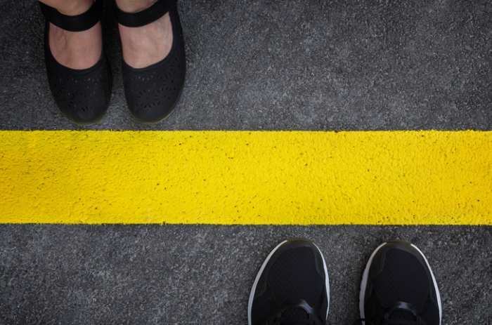 two pairs of feet stand on opposite sides of a thick yellow line painted on pavement