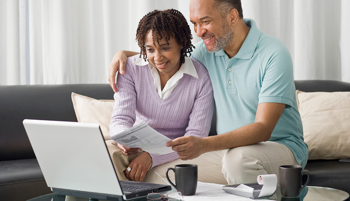 a husband and wife look at documents together in front of a laptop