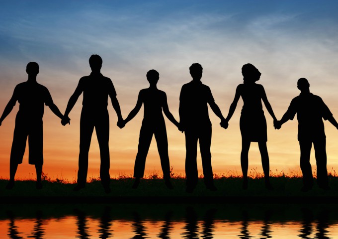 a diverse group of people hold hands in a line, silhouetted against a sunset