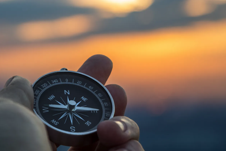 a hand holds a compass against a sunrise background