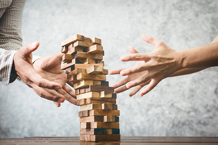 a tower of interlaced wooden blocks starts to topple as two hands reach out to save it