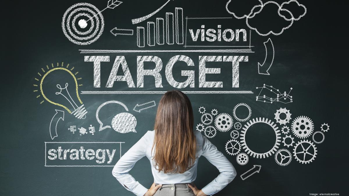a woman stands in front of a chalkboard covered in growth symbols and words, including "vision," "strategy," and lightbulbs and rising bar graphs