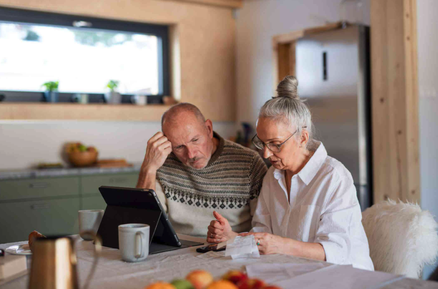 a worried middle-aged couple looks at their bank statements while sitting at their kitchen table