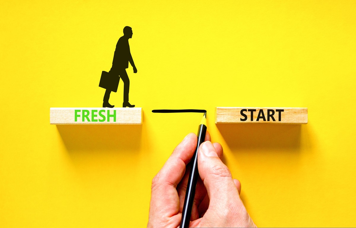 a silhouette of a businessman carrying a briefcase walks between two wooden shelves as a hand draws a line between them, representing a fresh start in a career