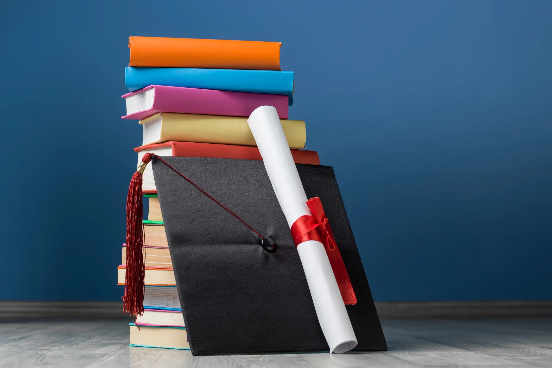 a stack of books with a rolled-up degree and mortarboard
